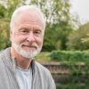 Man in his 60s looking towards camera wearing a grey cardigan, focus on head and shoulders